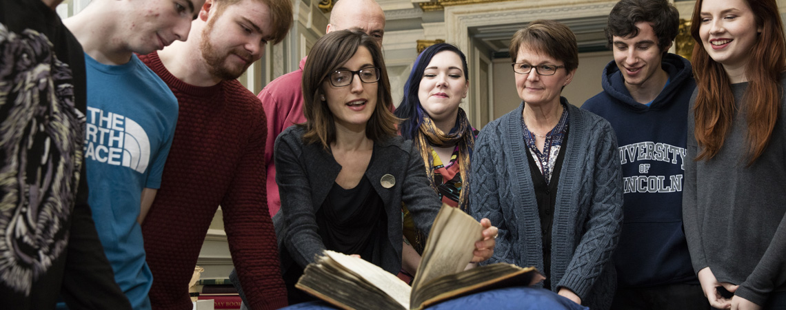Students and a lecturer looking at a medieval manuscript in the Wren Library at Lincoln Cathedral