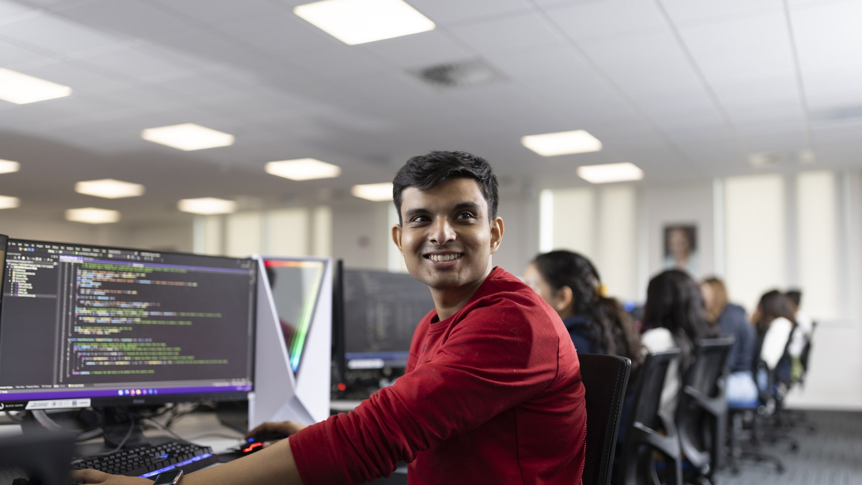 A student at a computer smiles at the camera